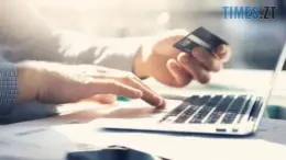 руки: одна тримає банківську картку, а інша вводить текст на клавіатурі комп`ютера