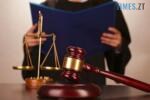 судовий молоток та ваги на фоні чоловіка у судовій мантії з папкою в руках