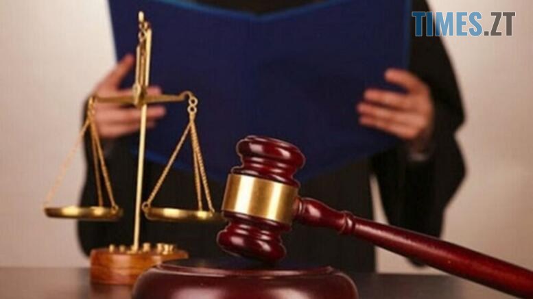 судовий молоток та ваги на фоні чоловіка у судовій мантії з папкою в руках