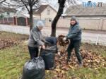 двоє людей прибирають опале пожовкле листя у сквері в Житомирі